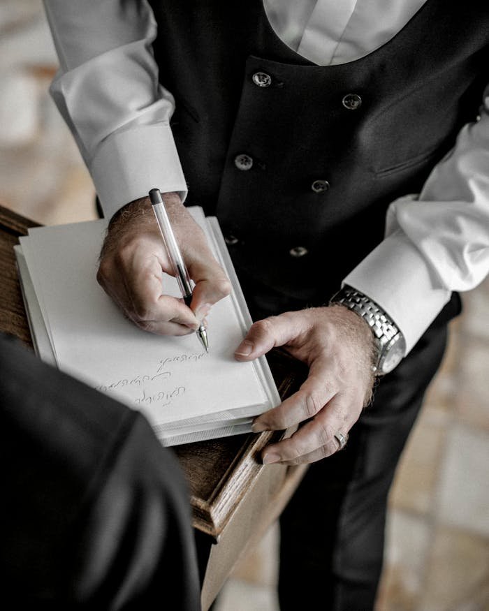 services-04 Close-up of a man in formal attire signing a document during a wedding ceremony.