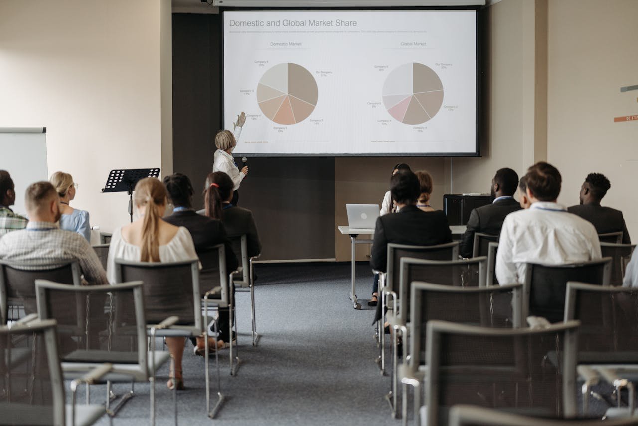 why-choose-us Business conference with diverse audience and speaker presenting market data.